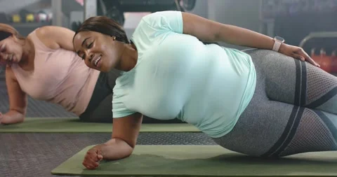Diverse female workout partners doing left-side plank on mats at gym following Stock Footage 343098749