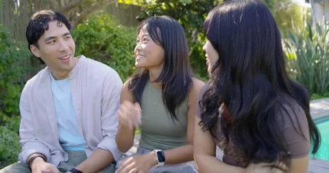 Diverse friends on bench by backyard pool, left man starting chat, laughing and Stock Footage 335212264