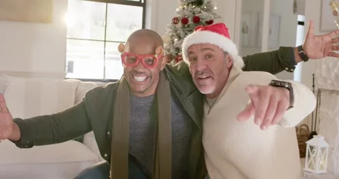 Diverse friends on couch by Christmas tree laughing while man in Santa hat Stock Footage 344654764