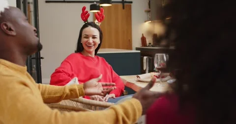 Diverse friends at holiday dinner sharing stories at table with antler headband Stock Footage 338325647