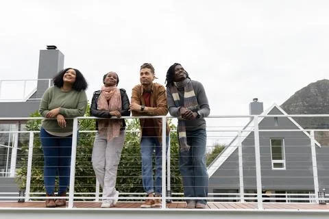 Diverse friends leaning on cable railing on raised deck, wearing sweaters Stock Photos