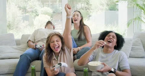 Diverse friends playing game on couch holding controllers popcorn cheering after Stock Footage 335867697