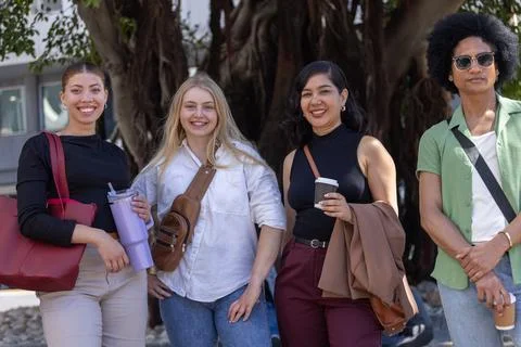 Diverse friends posing and smiling by large tree at campus plaza, holding Stock Photos