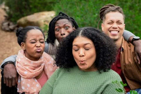 Diverse friends posing while puckering lips in garden area next to large rock Stock Photos