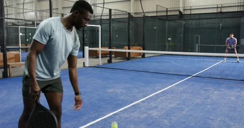 Diverse friends practicing padel on blue court bouncing ball, serving over net, Видео 337025412