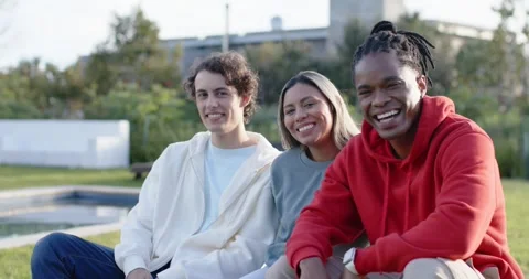 Diverse friends responding to camera, smiling and leaning on bench by pool, red Stock Footage 346180082