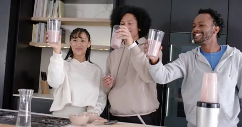 Diverse friends seeing ring light raising glasses of pink smoothie at kitchen Stock Footage 345590173