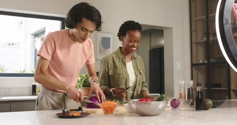 Diverse friends slicing cabbage on kitchen island under ring light while Vidéo 344253718