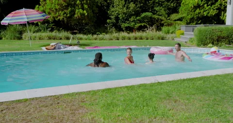 Diverse friends stepping back at backyard pool, jumping into water using float Video stock 310369315