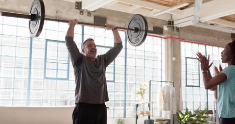 Diverse friends training in loft gym, coach cueing man pressing barbell Stock Footage 337289291