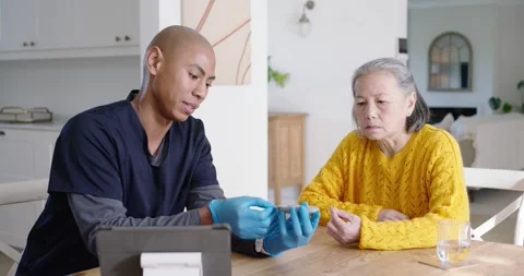 Diverse gloved caregiver testing Asian senior's finger with glucometer, checking Stock Footage 344670054