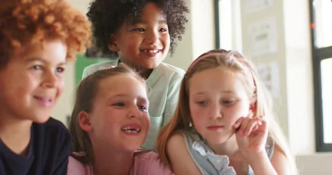 Diverse group of children leaning toward tablet playing funny clip at school, Stockbeeldmateriaal 337097464
