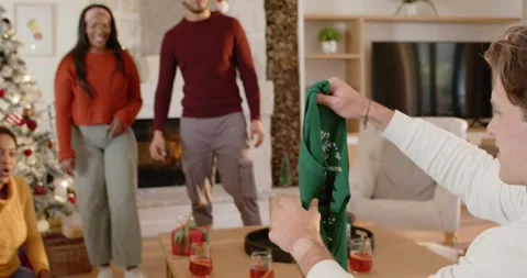 Diverse group at Christmas watching man opening box lifting green festive jumper Stock Footage 344230338