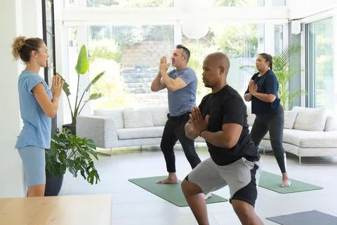 Diverse group following Indian instructor leading yoga on green mats by glass Stock Photos