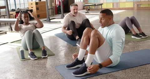 Diverse group following man on blue mat leading tempo, doing crunches in gym for Stock Footage 337286791