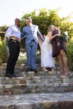 Diverse group of four posing on stone steps under pergola, in suits, dresses, Stock Photos