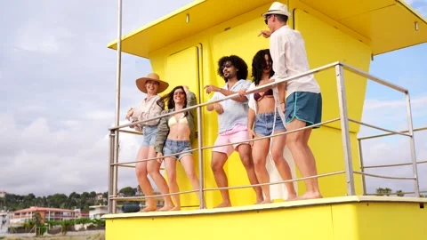Diverse group of friends dancing together on a yellow lifeguard tower Stock Footage 335875294