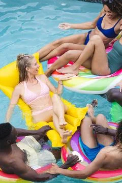 Diverse group of friends enjoy a pool party, lounging on colorful floaties Stock Photos