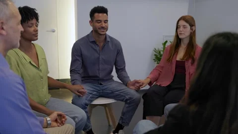 Diverse group holding hands with eyes closed while praying for support Stock Footage 345095776