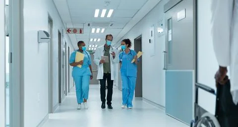 Diverse group of male and female doctors wearing face masks walking looking at Stock Photos