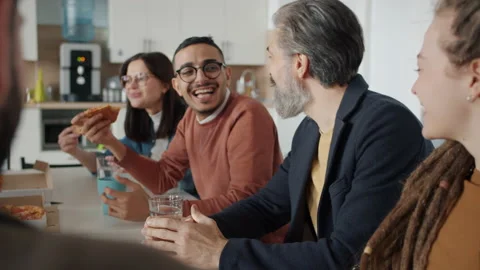 Diverse group of people coworkers talking and laughing eating pizza in workplace Stock Footage