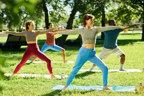Diverse Group Practicing Yoga Warrior Pose in Park Foto stock