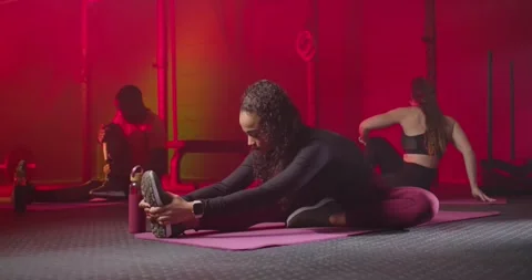 Diverse gym group during warmup stretching on mats, center woman holding shoe on Stock Footage 337730830