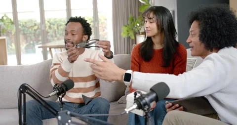 Diverse hosts on sofa right man gesturing with tablet urging left man checking Stock-Footage 345607768