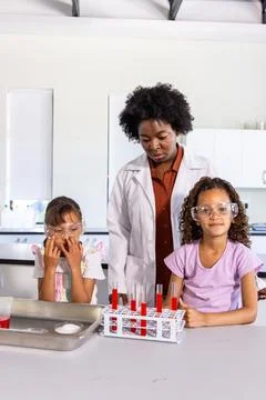 Diverse instructor guiding two child students at school lab with test tubes, Stock Photos