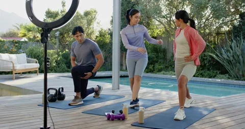 Diverse instructor stepping between mats guiding two clients doing lunges on Stock Footage 335907022