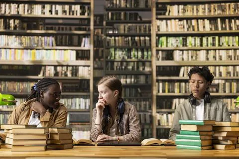 Diverse learners discuss study notes around open books at library table 写真素材