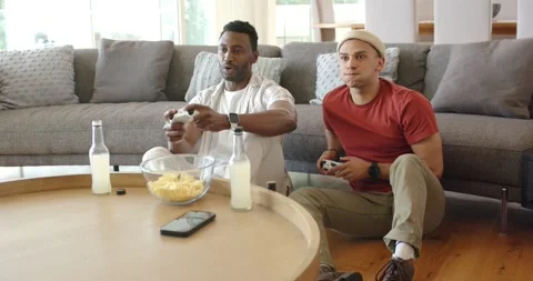 Diverse male friends reaching for controllers at home playing game for fun then Stock Footage 342492959