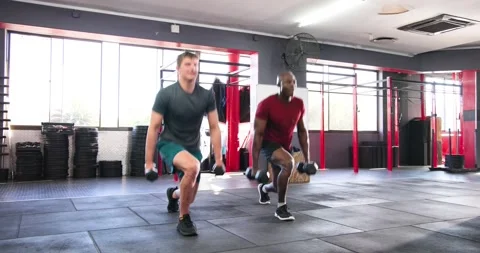 Diverse male partners performing alternating lunges with dumbbells in crossfit Stock Footage 337537037