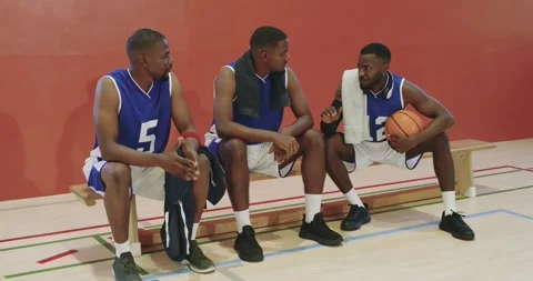 Diverse male partners taking break on bench at gym court discussing play Stock Footage 341089088
