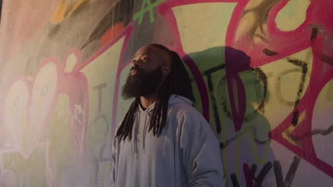 Diverse Man with Dreadlocks and Beard Leans Against Downtown Wall at Sunset Stock Footage 270399335