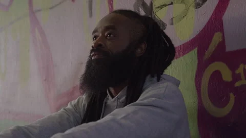 Diverse Man with Dreadlocks and Beard Looks up by Downtown Wall at Sundown Stock Footage 270399724