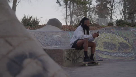 Diverse Man with Dreadlocks and Beard Sits Texting on Cell Phone at Skate Park Stock-Footage 270400173