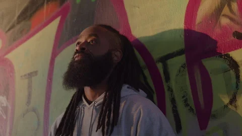 Diverse Man with Dreadlocks Looks up While Leaning Against Downtown Wall at Stock Footage 270399392
