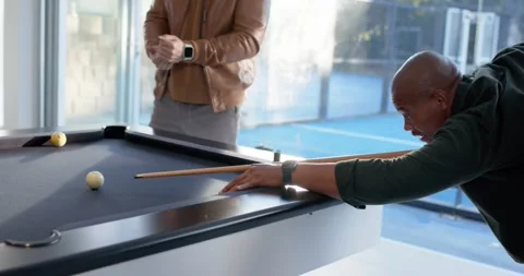 Diverse men around pool table watching man in pullover lining up, striking cue, Stock Footage 342033337