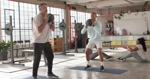 Diverse men following instructor cue, holding medicine balls, squatting in loft Stock Footage 337286765