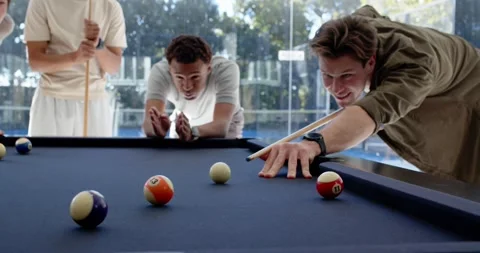 Diverse men guiding right player lining up, striking cue, balls rolling on navy Stock Footage 342066854