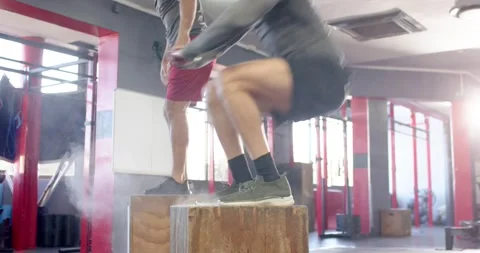 Diverse men performing alternating box jumps after partner landing on plyo boxes Stock Footage 336609082