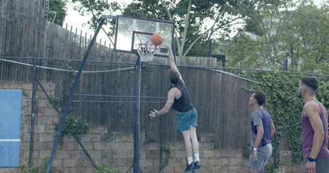 Diverse men playing backyard hoop, shooter in black tank dribbling past Stock Footage 342085028