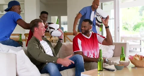 Diverse men on sofa reacting to beer-carrying friend passing VR sets while using Stockbeeldmateriaal 340969561
