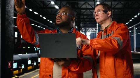 Diverse operators use laptop to coordinate production activity on factory floor Stock Photos