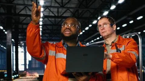 Diverse operators use laptop to coordinate production activity on factory floor Stock Photos