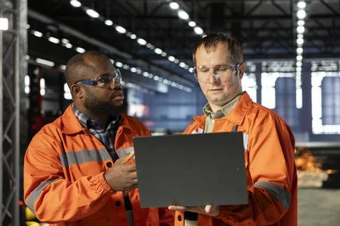 Diverse operators use laptop to coordinate production activity on factory floor Stock Photos