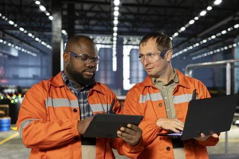 Diverse operators use laptop to coordinate production activity on factory floor Stock Photos