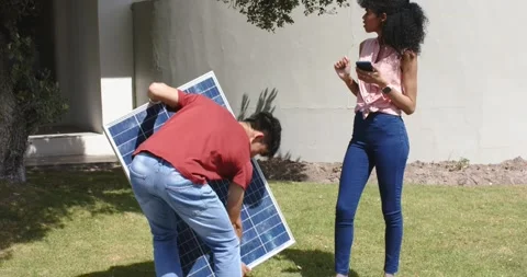 Diverse pair entering yard with solar panel, adjusting then standing it while Video stock 340972969