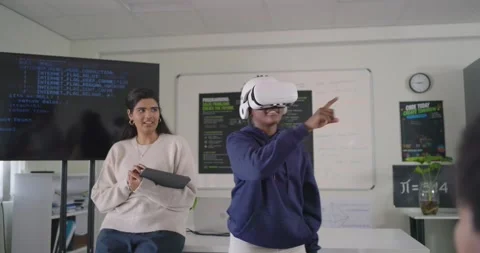 Diverse peers in tech lab demo watching African American teen male demoing VR Stock Footage 340811524